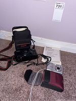 Photo showing both cameras (Pentax Optio E40 and Canon Sure Shot Zoom-S), their cases, and the Pentax Optio E40 quick start guide on carpet floor.