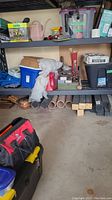 Shelving containing various tools, building supplies including wooden boards, PVC pipes, tool boxes, hand tools, a watering can and other items.