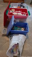 View showing three plastic storage totes with craft supplies including glue, paint, brushes inside, and a white plastic bag in front