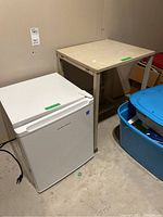 Mini fridge and rolling table placed side by side in basement against wall, showing overall condition and size.