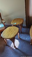 Two matching wooden end tables with shell-like leg carvings, seen side by side on carpet near chairs and curtain.