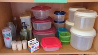 Multiple plastic food storage containers in various sizes and colors (clear, red, blue, green), toothpick holders, soap dispenser bottle, two small vases and floral decorated glass.