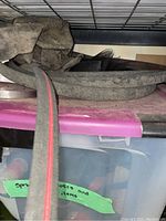 Photo showing garden hoses coiled and some screening material stored on a metal rack shelf.