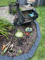 Photo showing the metal crane garden stake, blue and red bird solar garden stakes, solar flower stake, and four decorative mushroom stakes arranged in a garden bed with mulch and edged with stone blocks.