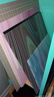 Stack of pink-purple swirl panel, turquoise panel, smoky black-tinted panel leaning against wall