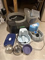 Photo showing multiple pet accessories including the Litter Roundup tray, containers, wire shelf, pet water fountain, metal canister, and bowls.