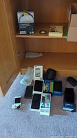 Five smartphone boxes on floor plus white iPhone and various accessories spread out