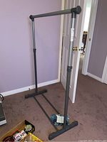 Full view of assembled portable clothing rack showing adjustable metal frame and caster wheels on a carpeted floor.