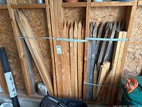 Photo showing multiple wooden stakes of different lengths and finishes secured together on a pegboard wall section in a garage area.