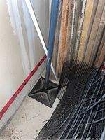 Kobalt 10x10 tamper leaning against a wall next to some rolls of black mesh and wood planks.