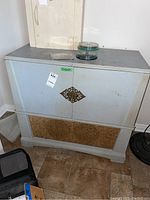 Photo of front and top of the vintage stereo cabinet showing wear, decorative metal plate on doors, cork bottom panel, and top items not included