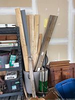 Wide shot of large plastic garbage can filled with various wood pieces and two brooms leaning on the right.