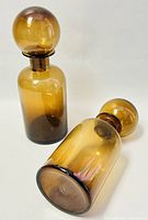 Two amber smoked glass decanters with spherical stoppers, one standing and one laying down showing base