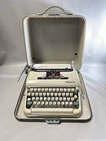 Full view of Olympia SM3 De Luxe typewriter in open light-colored hard case with handle, ivory colored body, showing keyboard and platen.