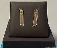 Front view of pair of tri-gold drop earrings displayed on black stand showing tri-colored gold with textured pattern
