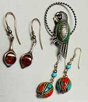 Photo showing both pairs of drop earrings and the parrot brooch together on a white fabric background.