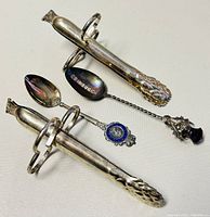Image showing the pair of vintage sterling silver asparagus tongs and two collectible spoons including the Edinburgh marked spoon and the blue enamel medallion spoon.