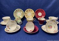 Three sets of Aynsley teacup and saucers in varied colors and patterns. Cups paired with matching saucers.
