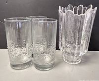 Three textured clear glass tumblers alongside one clear textured crystal vase with scalloped edge.