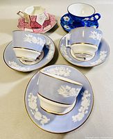 Three teacup and saucer sets arranged with two light blue Spode Copeland sets, one dark blue set, and one pink/white set in background