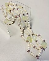 Close-up view of necklace displaying white baroque pearls, light green oval precious stones, and small purple beads.