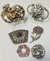 Overview of six vintage metal brooches displayed on white background showing size and design variety