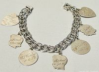 Full view of sterling silver bracelet with seven different etched charms including heart and shield shapes with names and dates.