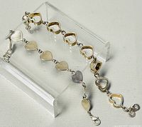 Photo showing two silver bracelets on clear acrylic display stand, one with solid hearts, the other with hollow hearts, both marked 925.