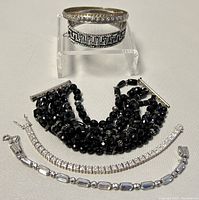 Overview of all five bracelets laid out, showing different styles including silver bangles and black bead bracelets with rhinestone tennis bracelets.
