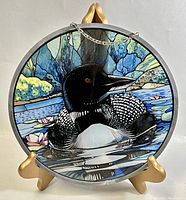 Front photo showing the stained glass wall art with a loon, water, and foliage in a circular metal frame on a gold stand.