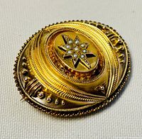 Oblique top view of oval gold brooch showing layered rope and bead details and central star motif with seed pearls.