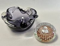 View of the purple blown glass ashtray/bowl and clear glass paperweight with brown spiral on a white surface.