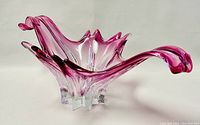 Front side view of the freeform pink and clear blown art glass bowl showing its curved user-facing edge and clear base feet.