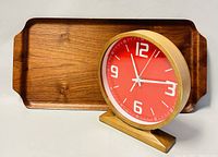 Photo showing battery-operated mantel clock with red dial, cream numerals, silver hands, and teak wood frame and base positioned on top of the tray.