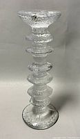 Front view of the clear, textured glass candleholder showing the six rings stacked on the stem and the flat base.