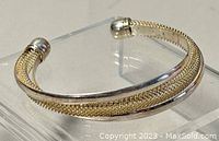 Front angled view of silver cuff bangle showing woven texture and polished band with rounded end caps.
