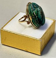 View of handmade 14K gold ring with large green carved scarab stone from angled side.