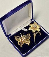 Two brooches in a blue velvet and satin-lined box, butterfly and flower design