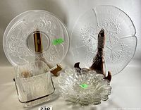 Four vintage glass servingware pieces displayed, showing two decorative platters, one floral bowl, and one square ice bucket with textured design.