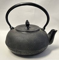 Front side view of the vintage black cast iron Chinese teapot showing its textured exterior surface, curved handle, lid with decorative finial, and short spout.
