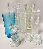 Full view of all 8 glass items including five vases with varied textures and three candleholders, set on white background.