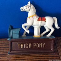 Side view of cast iron trick pony coin bank showing white pony on brown base with blue coin box and lever