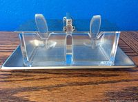 Front view of clear lidded condiment container with two compartments on metal tray
