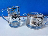 Photo of vintage glass creamer and sugar set with sterling silver floral design, set against blue and white backgrounds