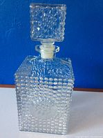 Front view of square crystal decanter with hobnail texture and square stopper, showcasing raised circular medallion design.