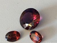 Close-up photo showing the three garnet gemstones on a white surface highlighting the deep red color and faceted cuts.