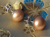 Close-up of pearl earrings showing round peach-colored pearls on sterling silver posts with large backs.