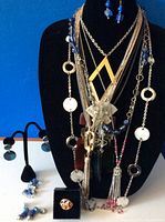 Front view of jewelry displayed on black bust and earring stand showing layered necklaces and earrings