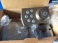 Photo of the exterior keypad lock with numeric buttons and key slot in the box, wrapped partially in plastic.