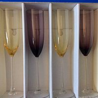 Four Lenox champagne flutes in box, two amber gold and two purple glass, 10 inches tall.